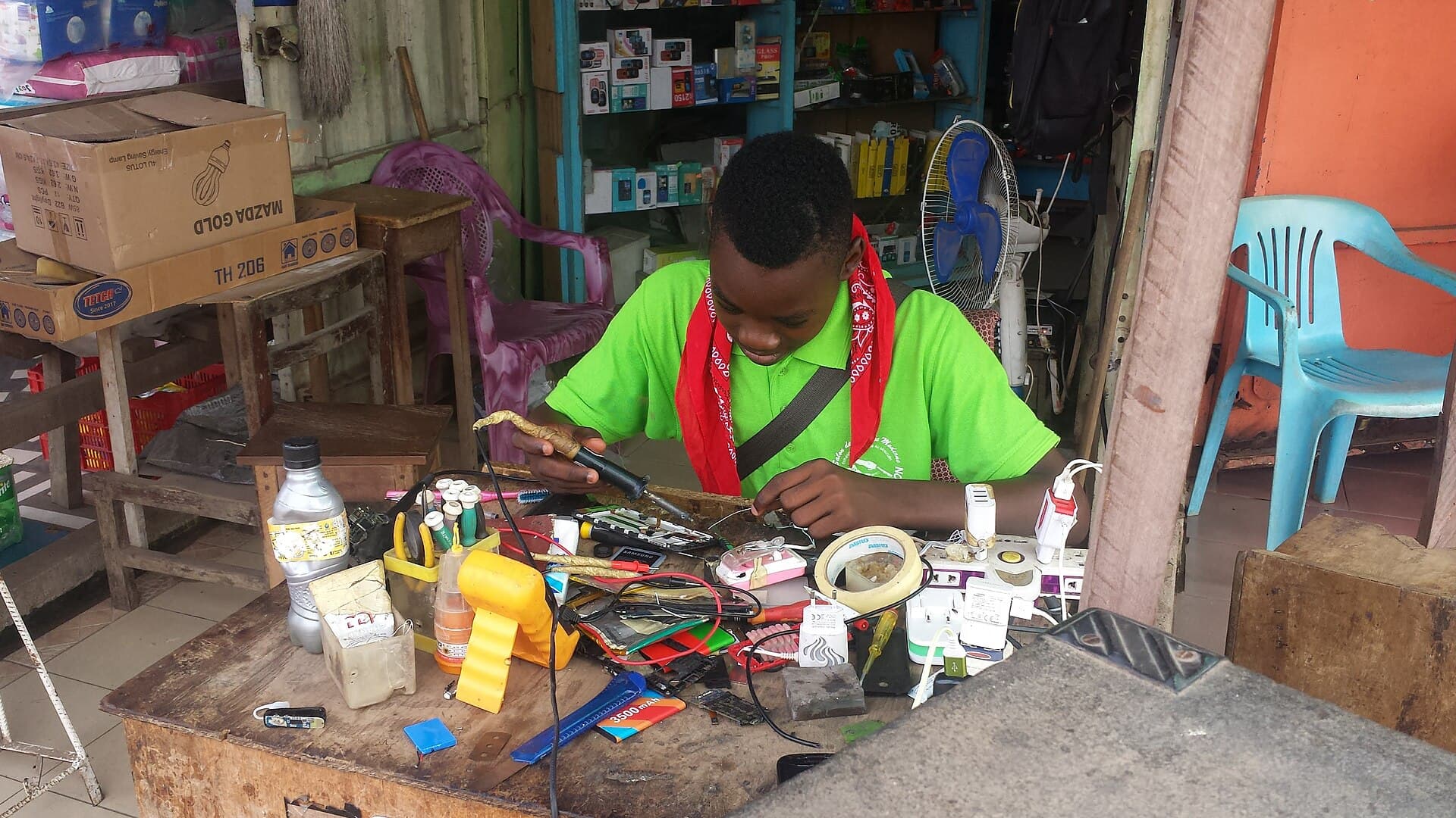 Technicien camerounais réparant un téléphone au fer à souder dans son atelier